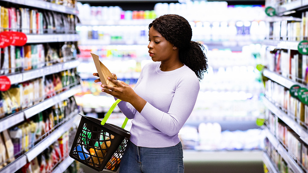 Young woman in grocery store aisle examines packaged food label.