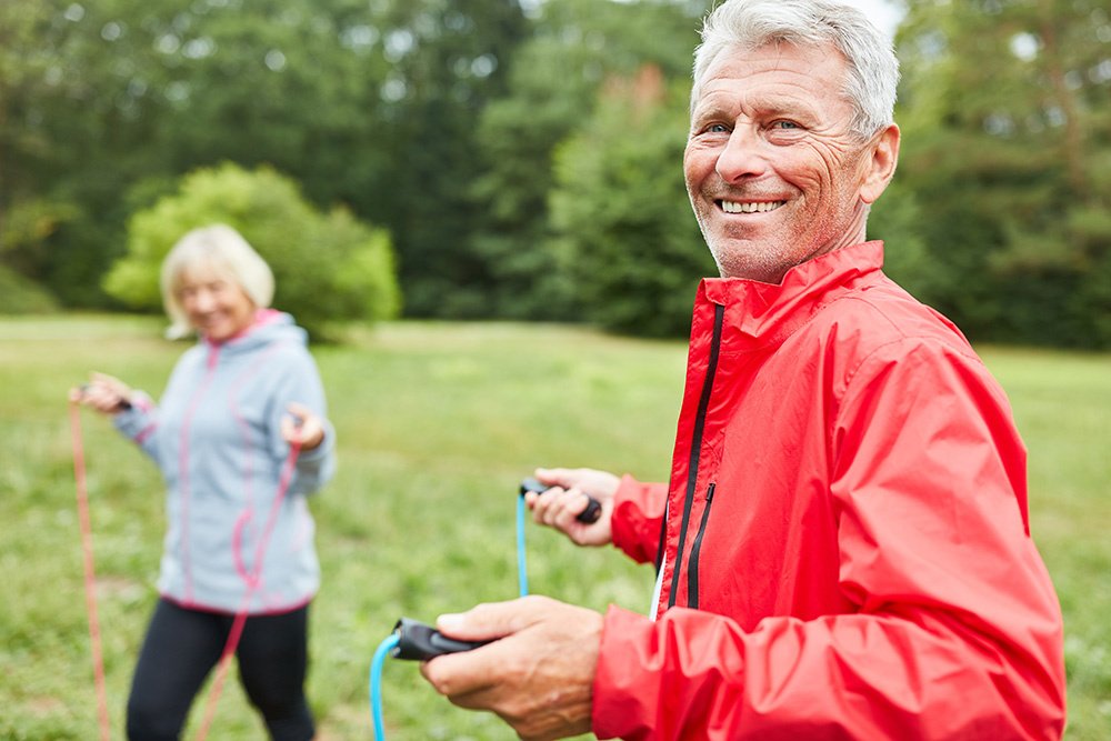 Senior man walks outdoors holding a jump rope. Article is about cancer screenings for older adults.